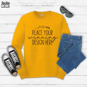 May include: Mustard yellow long-sleeve shirt with the text "PLACE YOUR WINNING DESIGN HERE". The shirt is paired with blue jeans and black and white sneakers. Sunglasses are also included in the image.