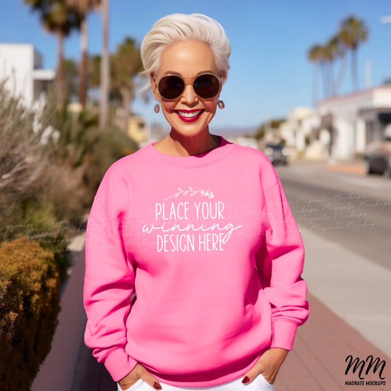May include: A pink sweatshirt with the text "Place your winning design here" in white. The sweatshirt is being worn by a person outdoors.