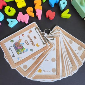Puede incluir: Un conjunto de bloques de letras de madera de colores y un portapapeles marr&oacute;n con una hoja de papel blanca que dice "Mi lista de la compra" con un carrito de la compra de dibujos animados lleno de comestibles.