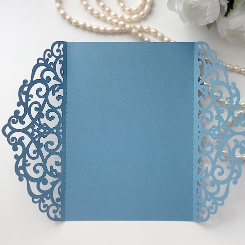 May include: A light blue invitation envelope with a delicate, intricate lace design cut out around the edges.