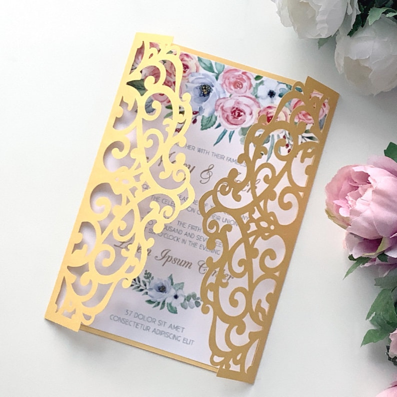 May include: Gold laser cut wedding invitation with a floral design. The invitation features a delicate, intricate pattern with a floral motif. The invitation is perfect for a romantic wedding.