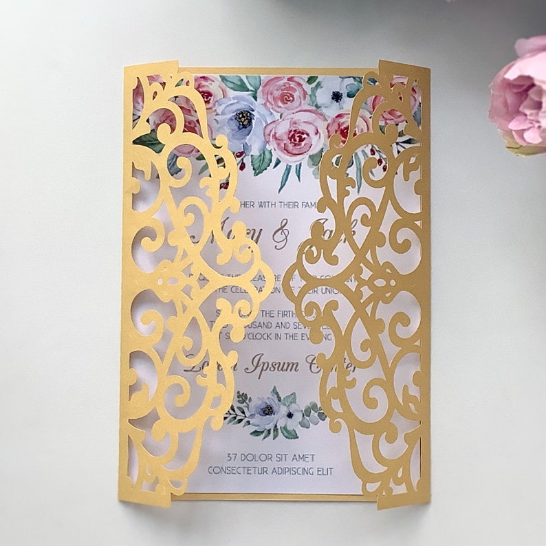 May include: Gold laser cut wedding invitation with a floral design and the text "HER WITH THEIR FAM & ZIR UNIO THE FIRTH SAND AND SEV CLOCK IN THE EVNG Ipsum & 37 DOLOR SIT AMET CONSECTETUR ADIPISCING ELIT"