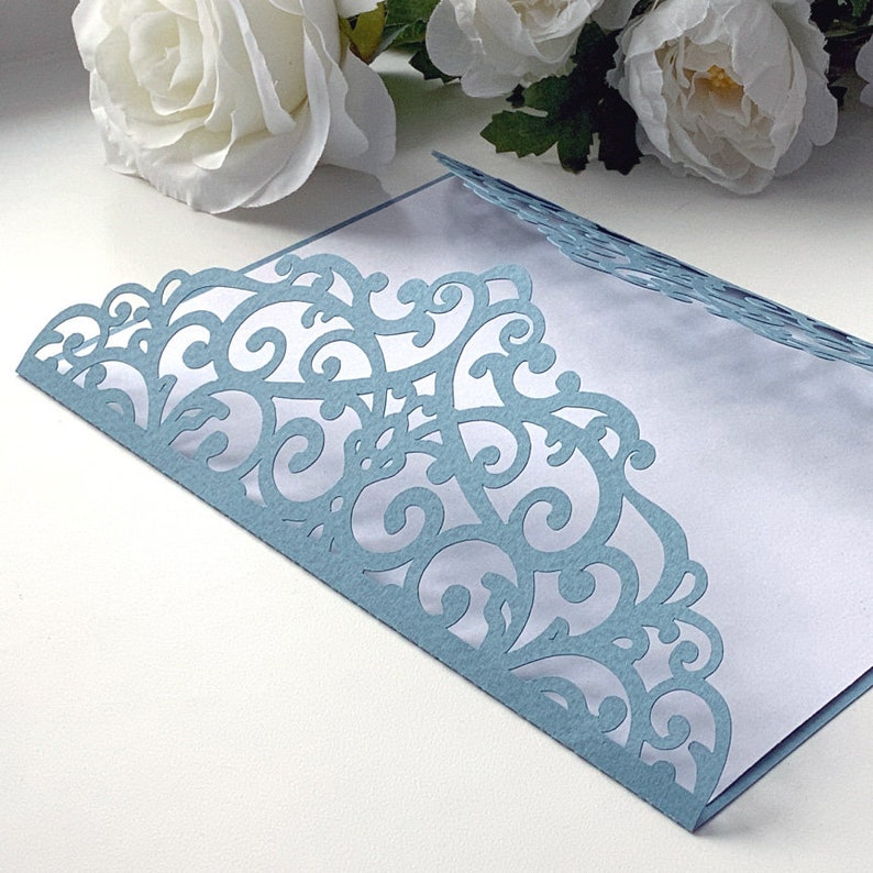 May include: A light blue envelope with a delicate, intricate lace design cut out around the edges. The envelope is open and the inside is white.