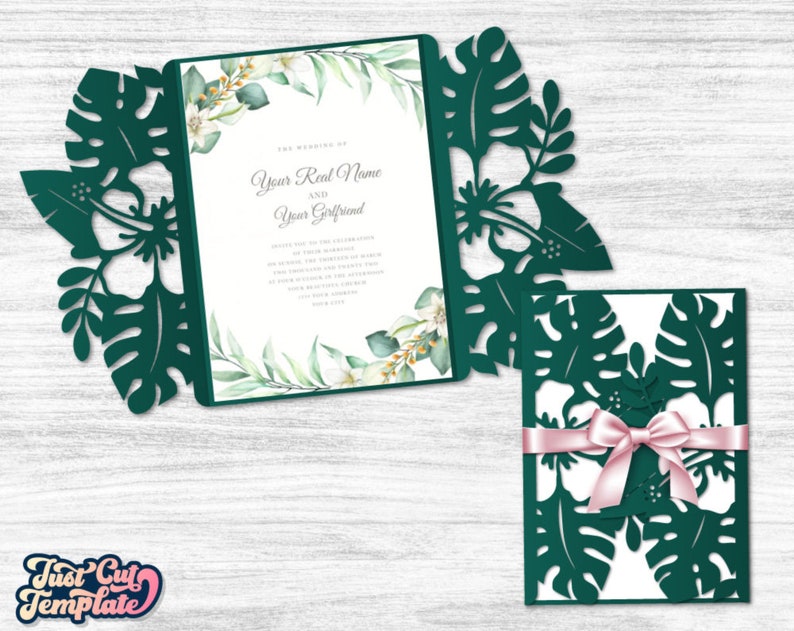 May include: A green and white wedding invitation with a tropical leaf design. The invitation is folded in half and has a white envelope with a pink ribbon.