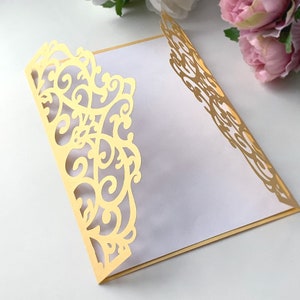 May include: A gold-colored, laser-cut, decorative envelope with a delicate, intricate floral design. The envelope is folded and has a white interior.