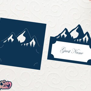 May include: A blue mountain silhouette with trees, a place card with the text "Guest Name" for a wedding or party.