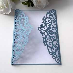 May include: A light blue laser cut invitation envelope featuring a delicate, intricate floral design. The envelope is folded in half and has a white interior.