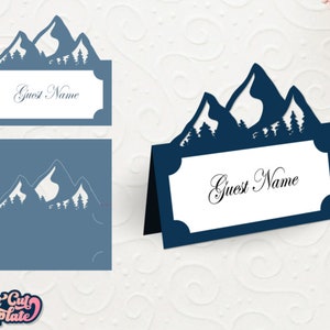 May include: A blue mountain range silhouette with trees, used as a place card holder. The card is white with the text "Guest Name" in black.