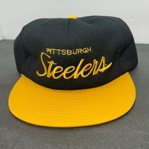 May include: Black and gold baseball cap with the text "Pittsburgh Steelers" embroidered in yellow on the front.