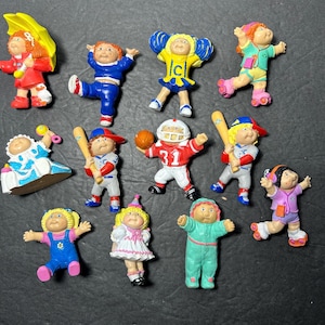 Peut inclure: Une collection de 12 figurines Cabbage Patch Kids. Les figurines sont toutes habillées de tenues différentes, dont une pom-pom girl, un joueur de baseball, un joueur de football américain, un bébé et un patineur à roulettes. Les figurines sont toutes en plastique et sont en bon état.