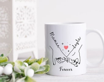 Puede incluir: Taza de cerámica blanca con un dibujo de línea negra de dos manos que se sostienen. El texto "Maman Layla Forever" está impreso en la taza.