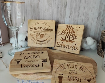 May include: Four wooden coasters with laser-engraved designs. The coasters feature a variety of designs, including a logo for "La Bel Kreation", a wedding-themed design with the text "Mr. & Mrs. Edwards", a design with the text "Le meilleur apéro c'est chez Vincent!" and a design with the text "Je peux pas j'ai apéro chez Lactt & Vince".