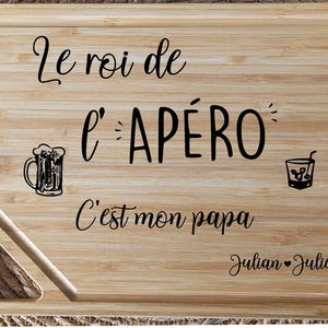 May include: A rectangular bamboo cutting board with the text "Le roi de l'AP&Eacute;RO C'est mon papa" and the names "Julian &hearts; Julie". The board features illustrations of a beer mug and a cocktail glass.