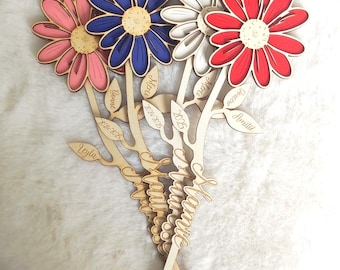 Puede incluir: Colección de decoraciones florales de madera en rosa, azul, blanco y rojo. Cada flor tiene una combinación de colores diferente y está unida a un tallo de madera con hojas. Los tallos están grabados con nombres y fechas.