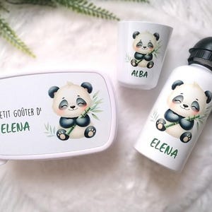 Può includere: Un portapranzo bianco, un bicchiere piccolo e una borraccia con tappo nero, ognuno decorato con l'illustrazione di un panda dei cartoni animati che tiene del bambù. Il portapranzo riporta il testo LE PETIT GOÛTER D' ELENA, il bicchiere ALBA e la borraccia ELENA.