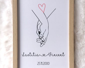 May include: A framed print with a black line drawing of two hands holding each other. The hands are intertwined and there is a red heart above them. The text "Laetitia & Vincent 25.11.2000" is below the drawing.