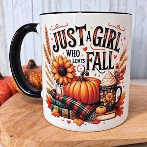 Peut inclure: Un mug en céramique blanche avec une anse et un bord noirs, orné d'un motif automnal coloré. Le design comprend une grosse citrouille orange, un tournesol, une écharpe à carreaux, des livres et un petit mug avec le texte JUST A GIRL WHO LOVES FALL.