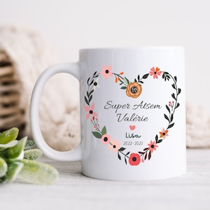 May include: White ceramic mug with a floral heart design. The heart features the text "Super Atsem Val&eacute;rie" and "Lisa 2022-2023".