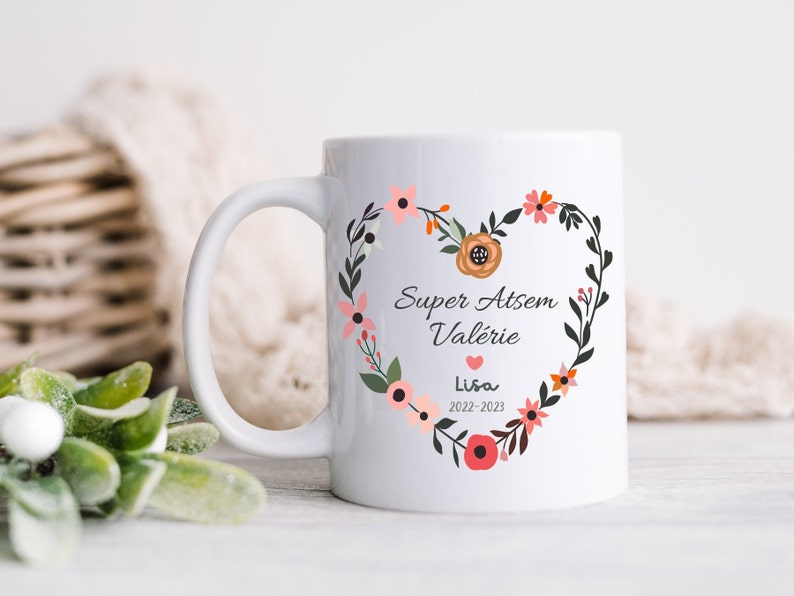 May include: White ceramic mug with a floral heart design. The heart features the text "Super Atsem Val&eacute;rie" and "Lisa 2022-2023".