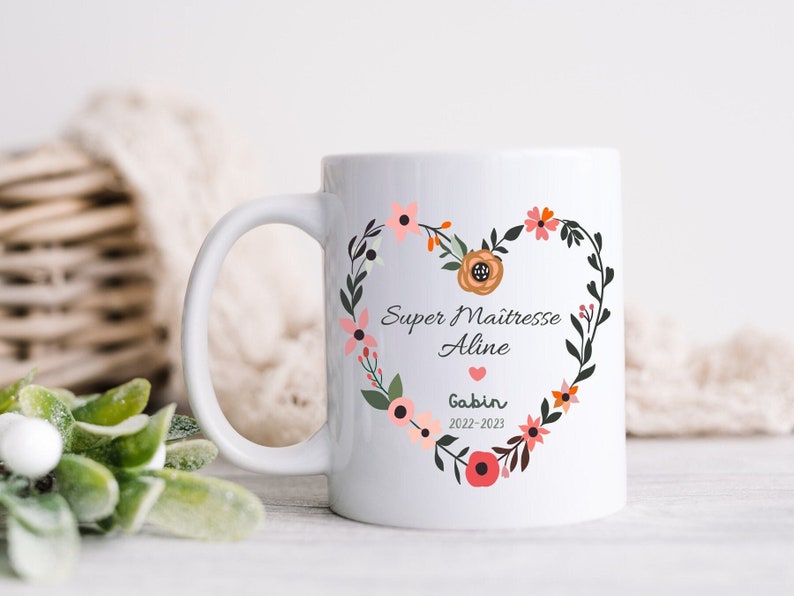 May include: White ceramic mug with a floral heart design. The heart features the text "Super Maitresse Aline" and "Gabin 2022-2023".
