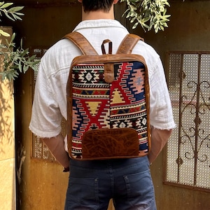 May include: A brown leather backpack with a colourful patterned fabric front panel. The fabric features geometric designs in shades of red, blue, yellow, and black.