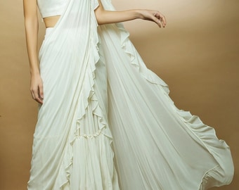 May include: A white ruffled saree with a sleeveless blouse. The saree has multiple layers of ruffles and is draped in a traditional style.