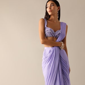 May include: A woman wearing a lavender saree with a matching embellished crop top. The saree is draped in a modern style with pleats and folds.