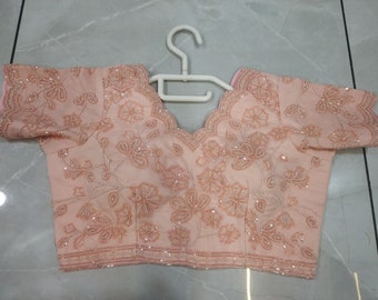 May include: A peach-coloured embroidered blouse with a scalloped neckline and short sleeves. The blouse is decorated with delicate floral patterns and sequins.