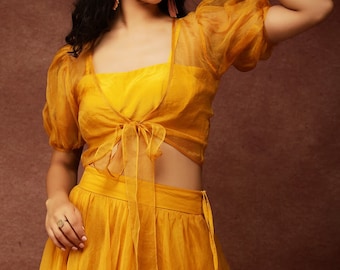 Designer yellow lehenga with ruffled trimming and a side tie. Included are a front tie-up top, a sleeveless bralette, and puff sleeves.