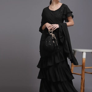 Puede incluir: Un vestido negro de maxi con volantes de varios niveles con un escote con volantes y mangas cortas. El vestido tiene una superposición transparente y se combina con un bolso negro con lentejuelas.
