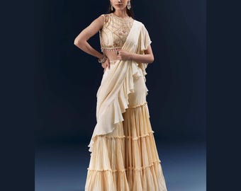 May include: An ivory-colored formal outfit featuring a heavily embellished, sleeveless top and a flowing skirt with multiple ruffled tiers. The ensemble includes a draped shawl, creating an elegant silhouette. The outfit is suitable for special occasions.