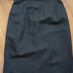 May include: A black skirt with a matching belt. The skirt is knee-length and made of a smooth fabric, possibly satin. The belt has a rectangular buckle. The skirt is a solid colour, with no visible patterns or embellishments.