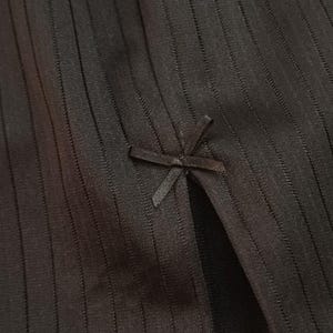 Op de afbeelding: Close-up van zwarte stof met verticale geribbelde textuur. Een kleine strikdetail bevindt zich bovenaan een spleet in de stof. De stof lijkt een zacht, mogelijk gebreid materiaal te zijn.