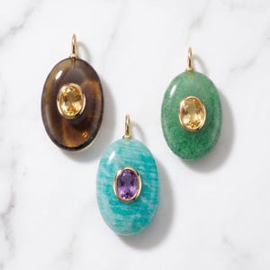 May include: Three oval pendants featuring polished gemstones in gold settings. One pendant is dark brown with a yellow citrine, one is bright green with a yellow citrine, and one is turquoise blue with a purple amethyst centre stone.