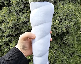 May include: A white plush toy shaped like a rolled joint with a green fuzzy top. The toy is held in a person's hand.