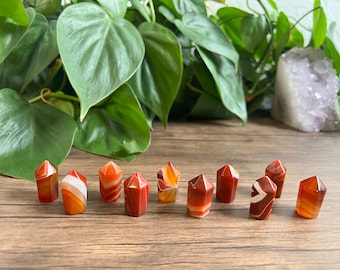 May include: A collection of ten carnelian crystal points with red, orange, and white banding. The points are arranged in a row on a wooden surface.