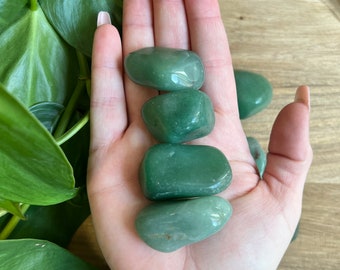 May include: Four smooth, green tumbled stones, likely jade, in a hand. The stones are various sizes and shapes.