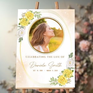 May include: A white memorial sign with a gold frame and a photo of a woman in a circle. The sign has yellow and white flowers and the text "Celebrating the life of Daniela Smith Oct 18, 1989 - March 5, 2026".