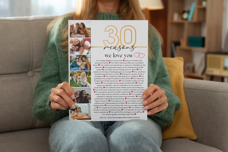 May include: A white card with gold lettering that reads "30 reasons we love you" with two red hearts. The card has a collage of photos of people smiling and laughing. The card is being held by a person's hands.