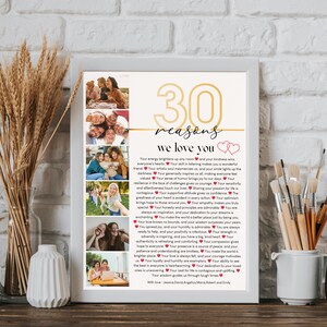May include: A white framed print with a gold number 30 and the words "30 reasons we love you" in a gold font. The print features a collage of photos of people and a list of reasons why they are loved. The print is on a wooden table with a vase of wheat stalks and a white vase with paintbrushes.