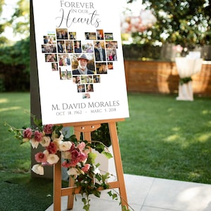 Pu&ograve; includere: Un cartello commemorativo su un cavalletto di legno, con un collage di foto a forma di cuore. Il cartello recita "Forever in Our Hearts" sopra le foto e include il nome M. David Morales e le date. Fiori rosa e bianchi adornano la base.