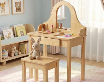 May include: A light wood children's vanity set with a matching stool. The vanity has a large arched mirror, a drawer, and is accessorized with makeup items. A stuffed bunny sits on the stool. The set is in a child's bedroom.