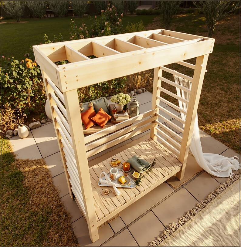 May include: A light-colored wooden outdoor canopy with a slatted roof and sides. Inside, there are pillows, a small table with drinks and snacks, and a bench. The canopy is set on a patio with a grassy background.