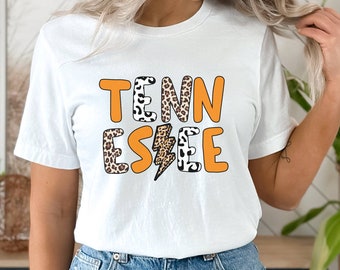 May include: White t-shirt with the word "TENNESSEE" in orange letters with a leopard print pattern and a lightning bolt graphic.