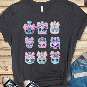 May include: A dark grey t-shirt featuring a design of nine pastel blue bottles with skull tops and pink bows. Each bottle has a different design on the skull.