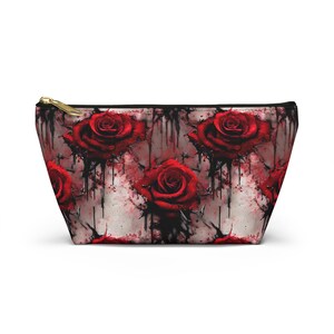 May include: A red rose print makeup bag with a white background and black dripping paint. The bag has a zipper closure.