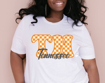 May include: White t-shirt featuring a graphic of the letters "TN" in orange and white gingham with the word "Tennessee" underneath.