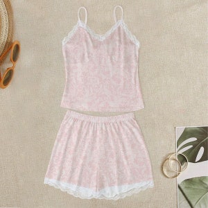 May include: A pink and white patterned pajama set with lace trim. The top is a sleeveless tank top with a V-neck and the bottom is a pair of shorts.