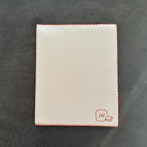 Op de afbeelding: Een crèmekleurige, rechthoekige portemonnee met oranje stiksels rond de randen. De portemonnee heeft een klein, oranje logo in de rechter benedenhoek met de initialen "JW".