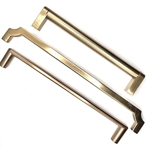 May include: Three brass-coloured cabinet pulls in different designs. The pulls have a rectangular bar shape with various end designs, including a straight edge, a curved edge, and a stepped edge. The hardware is set against a white background.